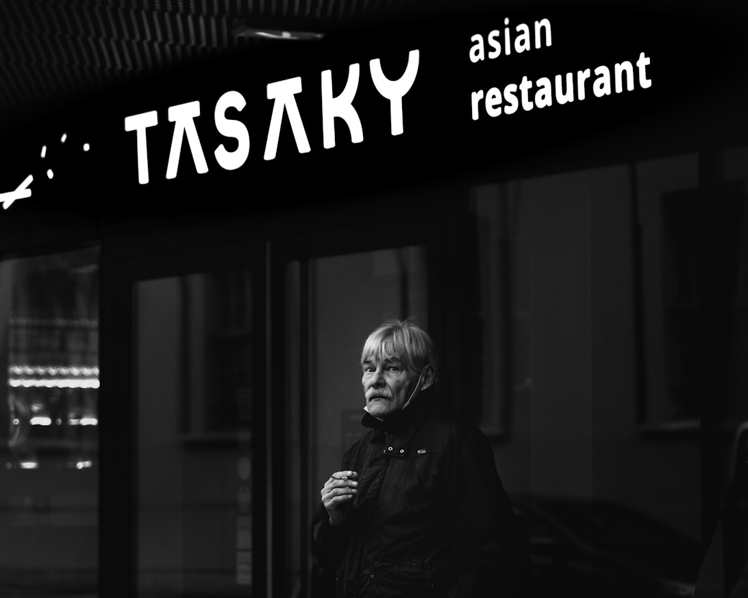 En svartvit bild av en person som står framför en asiatisk restaurang, vilket skapar en stämningsfull scen.