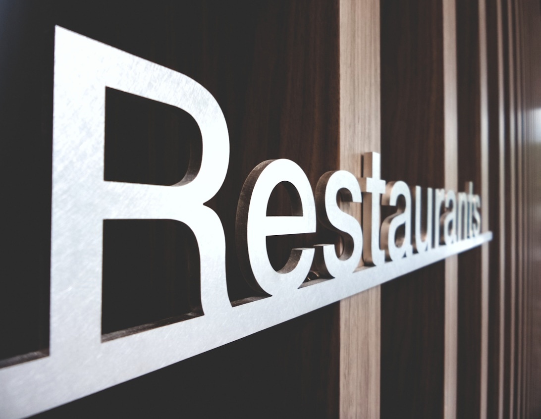 Närbild på vita metallbokstäver som stavar 'Restaurants' på en mörk vägg.